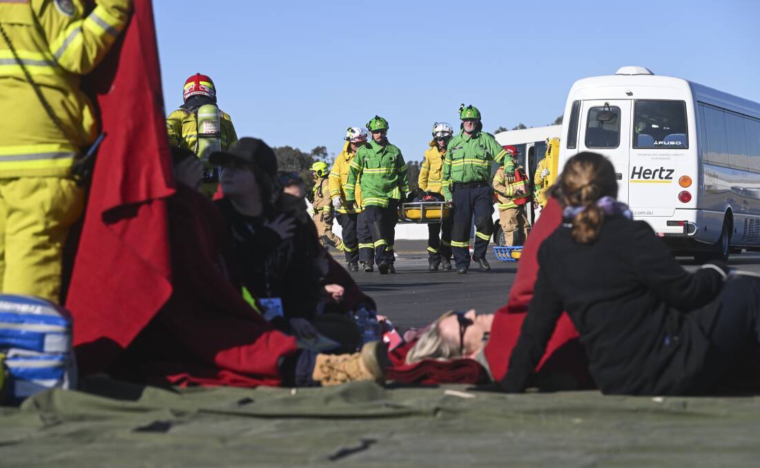 Passengers in the mock plane crash wait for assistance as VRA volunteers carry an injured passenger in a stretcher. Picture by Mark Jesser