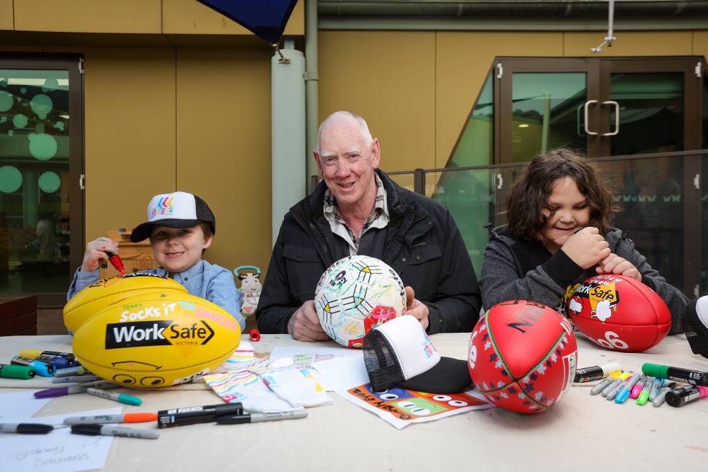 Chase Wallace, 5, Terry Greaves and Jackson Davis, 10, get to work on the footballs and netballs that will be auctioned at Ovens and Murray Football Netball League matches this weekend. Picture by James Wiltshire