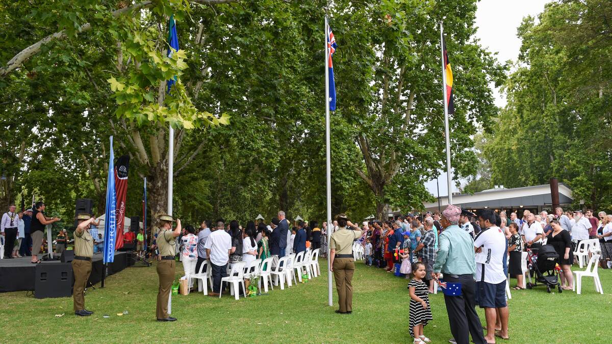 The crowd gathered from Albury's Australia Day formalities in Noreuil Park stand during the national anthem following the raising of flags.