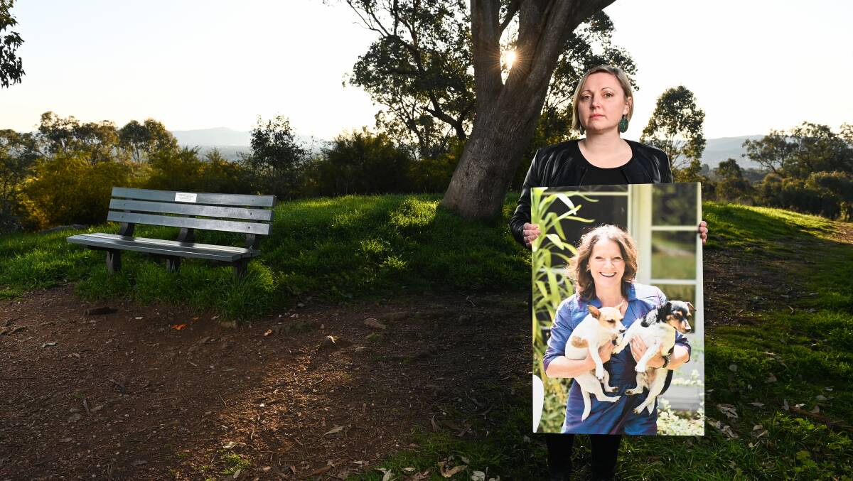 Lauren Black, pictured in August 2022, at the bench dedicated to her mother Elke, who can be seen holding her dogs in the giant photograph. 