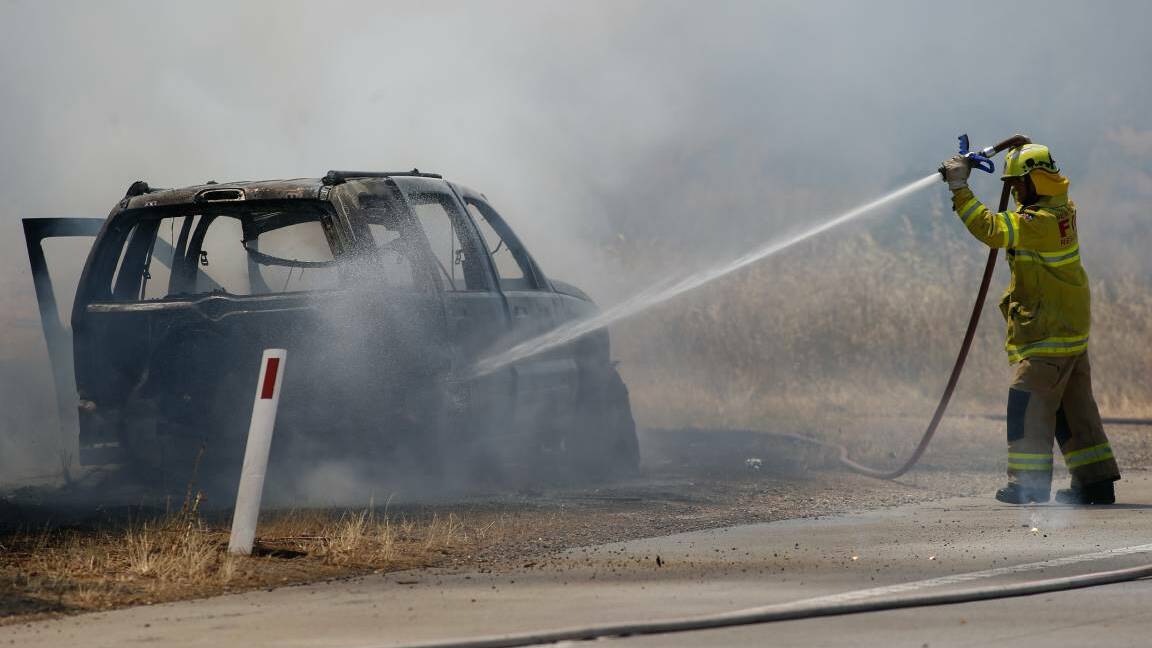 DESTROYED: A firefighter works to put out the car fire. Other firefighters worked on the blaze as it burnt through nearby bushland. Picture: MARK JESSER